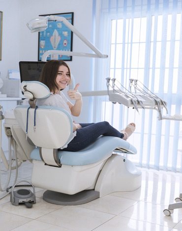 smiling-female-patient-sitting-chair-showing-thumb-up-dental-clinic (1)